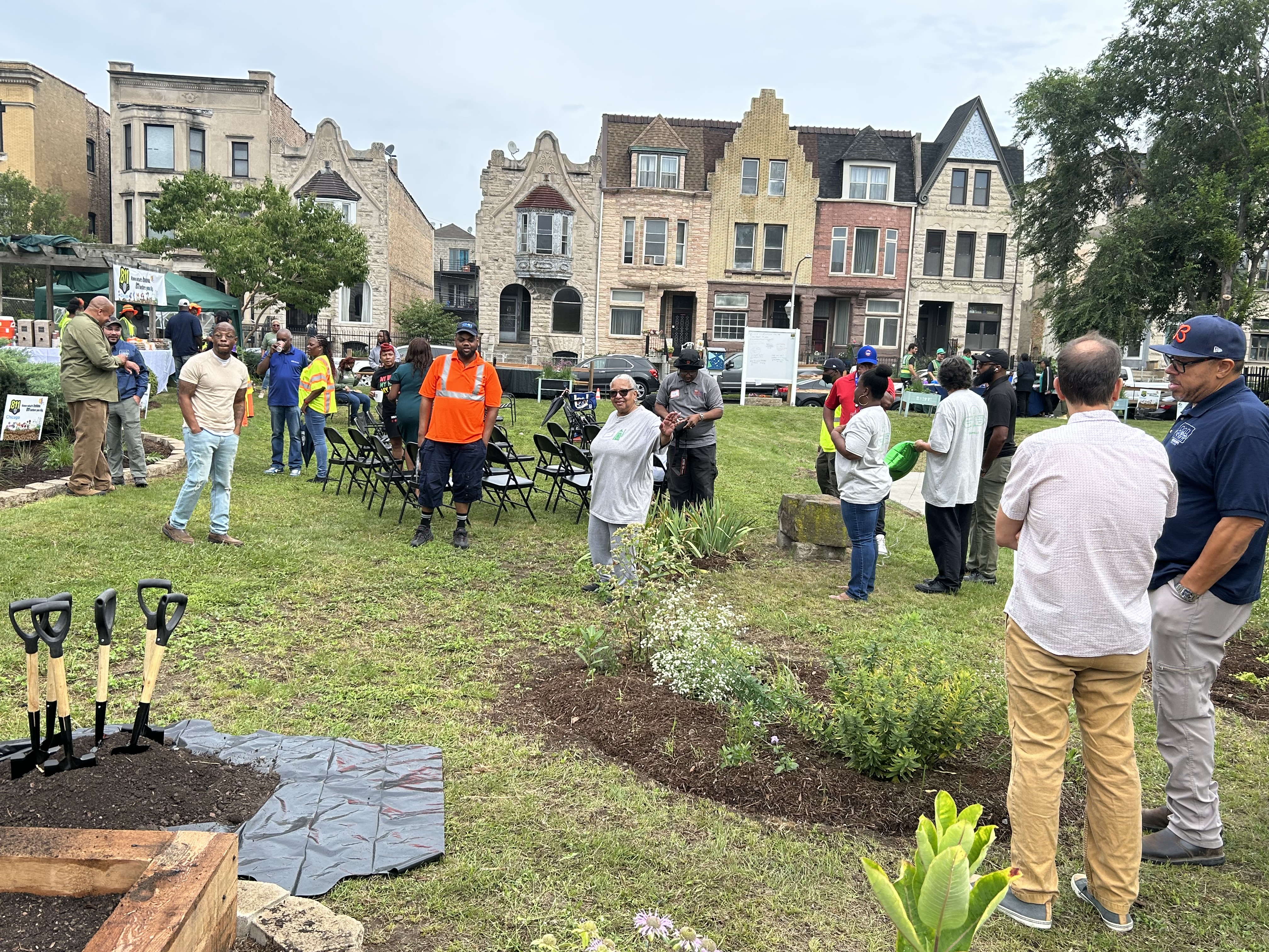 A group of about 25 standing and mingling in the community garden
