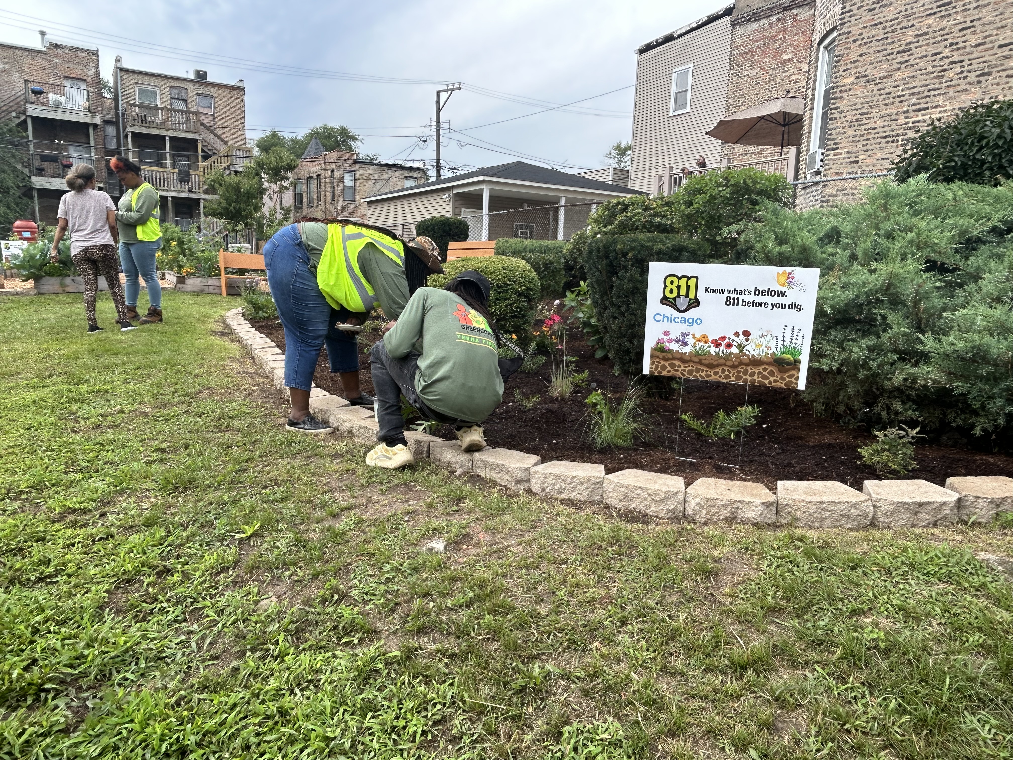 Two people tending to plants in a garden. An 811 Chicago sign is visible. 