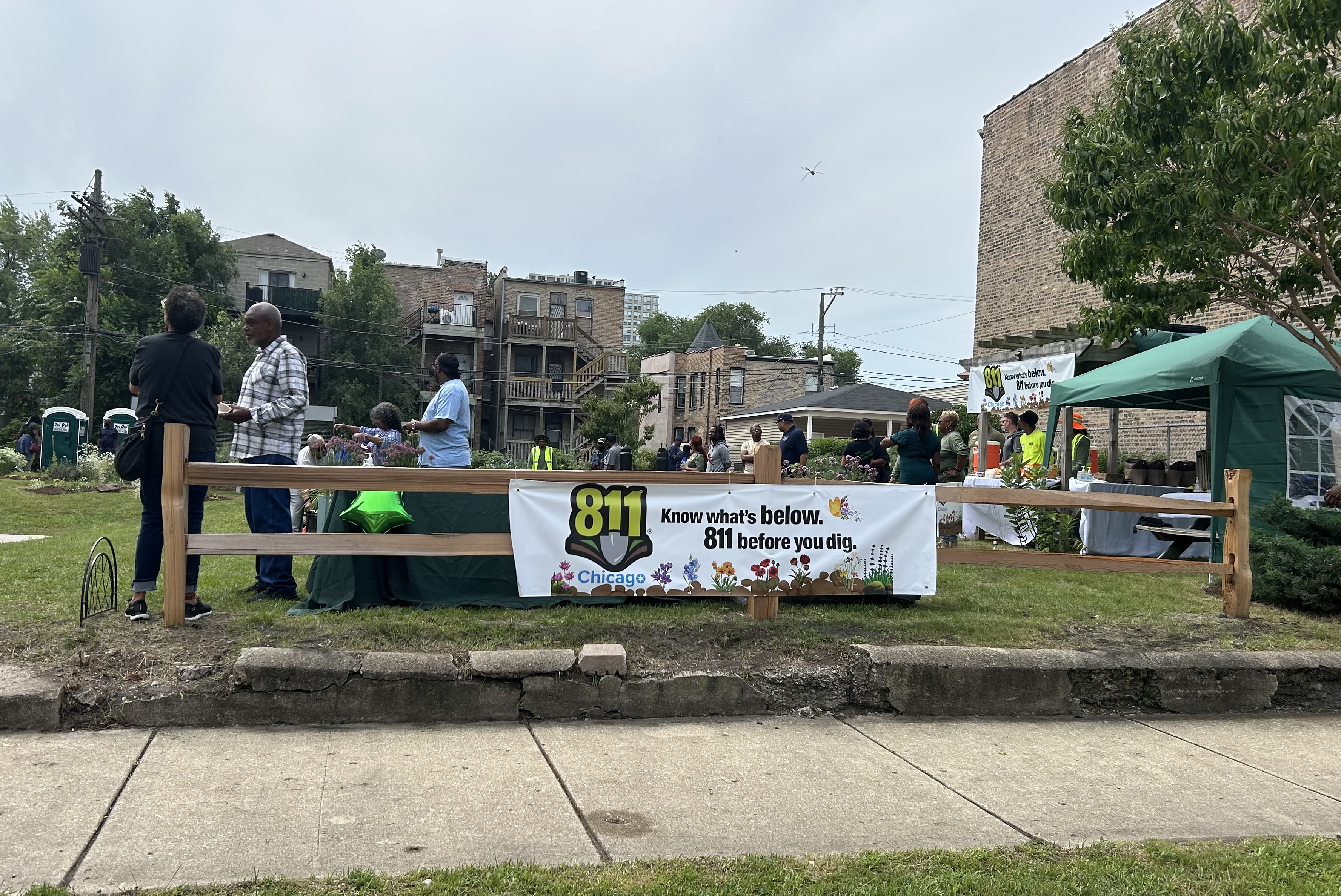 Photo of the community garden taken from outside the fence. There is a banner that days 811 Chicago on the outside of the fence.  