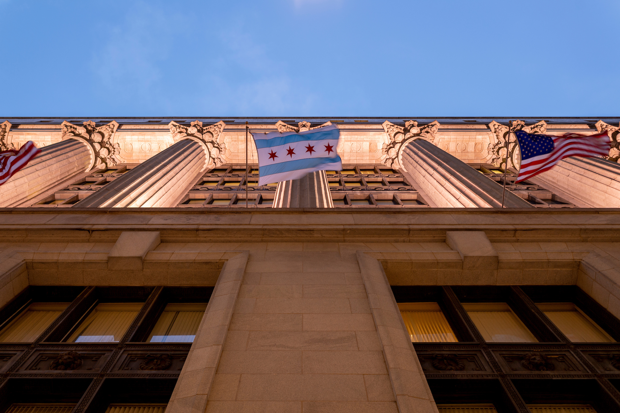 Photo taken of City Hall facing upward from ground-level looking at the City of Chicago flag.