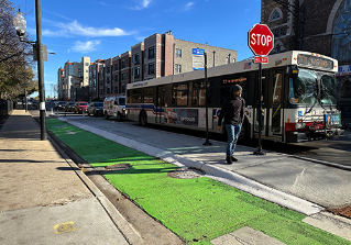 CTA bus stopped at bus stop with a concrete bus boarding island separating the travel lane from green painted bike lane.