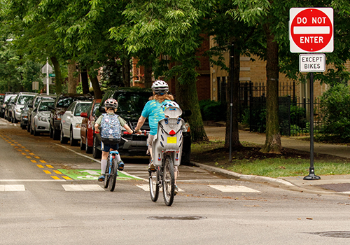 Family biking in a marked contraflow bike lane on a residential one way street. Signs say, do not enter except bikes. 