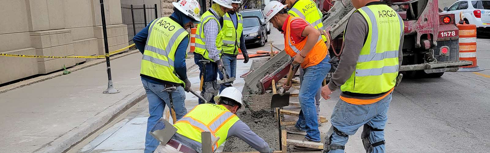 Group of construction workers gather around to shape concrete as it is poured. 