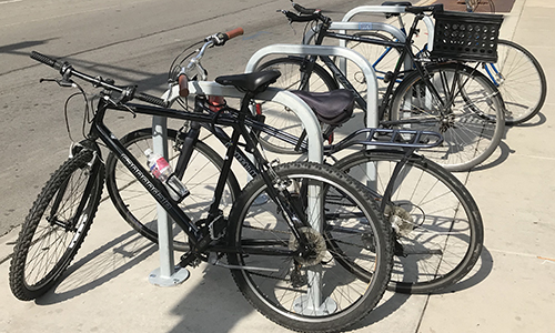 line of three bike racks on sidewalk with four bikes locked to them.