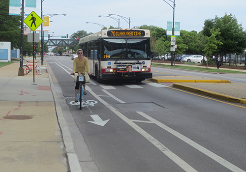 Person biking towards viewer in bike lane with CTA bus in vehicle travel lane