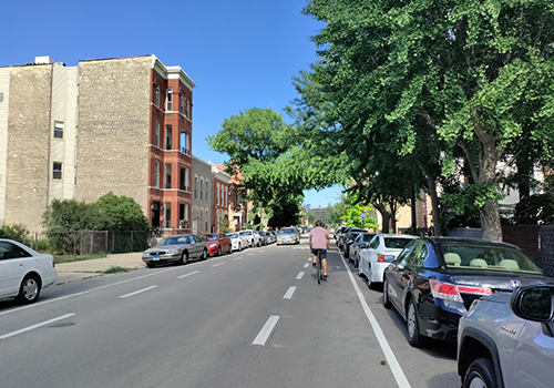 Person biking on road in advisory bike lane with dashed lines and cars in background