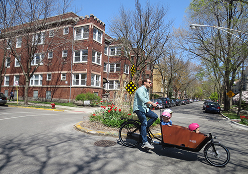 Adult and three children riding a cargo bike with a neighborhood traffic circle in the  background
