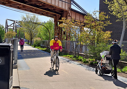 Person biking towards viewer on elevated trailand person walking with stroller away from viewer with trees surrounding