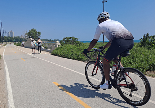 Person biking on Lakefront trail away from viewer with Lake Michigan visible in background.