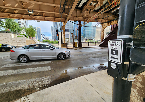 View of intersection with pedestrian push button visible in foreground