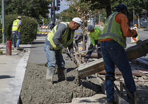 People wearing construction vests pouring concrete sidewalk