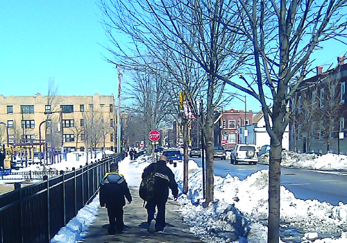 Adult and child wearing winter coats walking on sidewalk with snow shoveled to the side