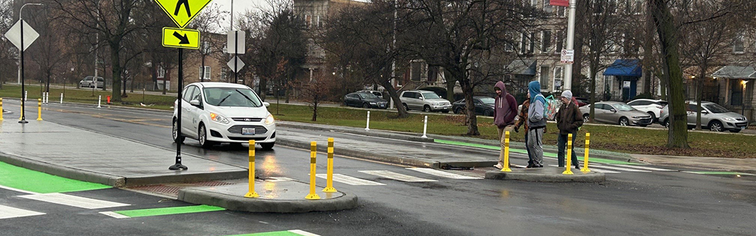 View of street with people crossing in crosswalk through concrete median