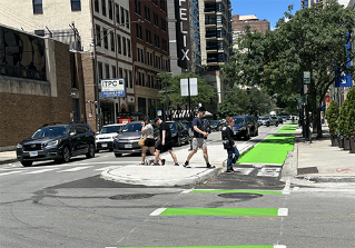 Person crossing street in crosswalk through concrete refuge island.