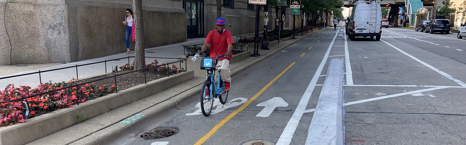 Person riding towards viewer on a blue Divvy bike in a bi-directional protected bike lane with concrete separating them from the vehicle travel lane