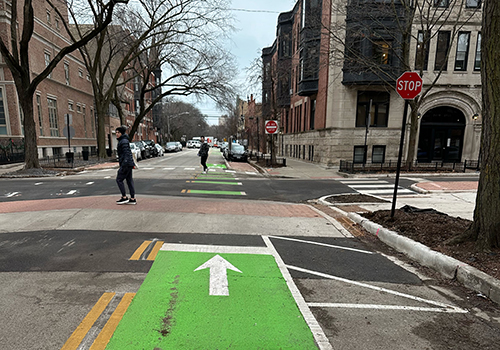 View of intersection with two people crossing the street on raised crosswalks