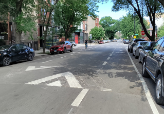 Person biking towards viewer in green painted bike lane separated from vehicle travel lane by concrete curb.