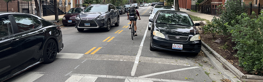 View of street with person biking in designated marked lane against the direction of vehicle traffic.