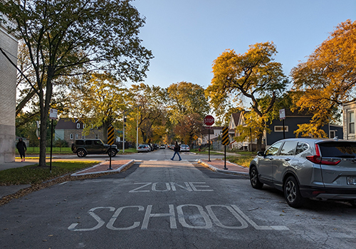 View of intersection with a person crossing the street in a crosswalk and school zone pavement markings visible