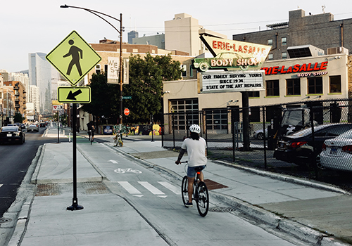 Person biking away from viewer in bike lane separated from vehicle travel lane by concrete curb.