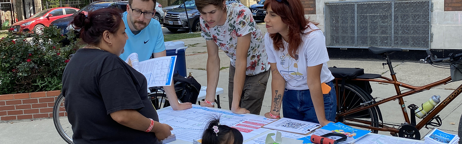 Group of people standing behind table with printed map displayed talking to community members