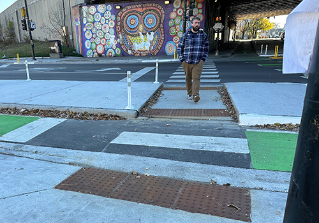 Person crossing street in crosswalk through concrete refuge island.