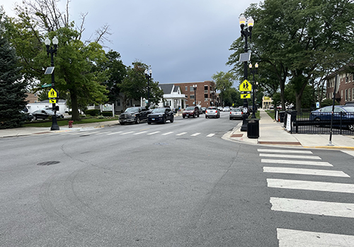 Roadway with rapid rectangular flashing beacon signs on both sides of a pedestrian crossing