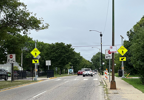 Roadway with rapid rectangular flashing beacon signs on both sides of a pedestrian crossing