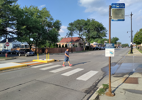 Person crossing the street in crosswalk passing through a concrete refuge island