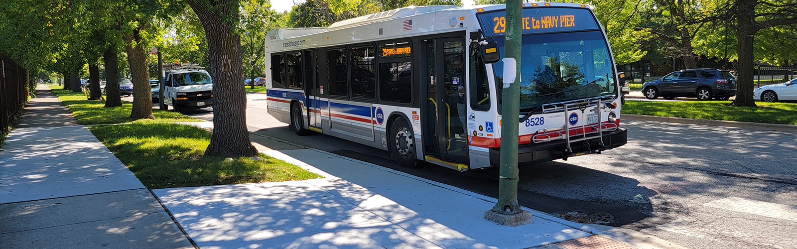 Bus stopping at signed stop with a fresh concrete sidewalk along parkway for boarding