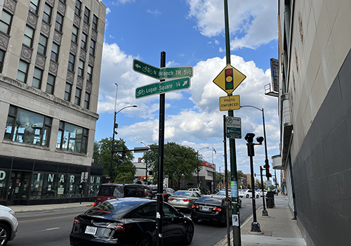 Red light camera sign and camera above street with vehicles queueing at the intersection