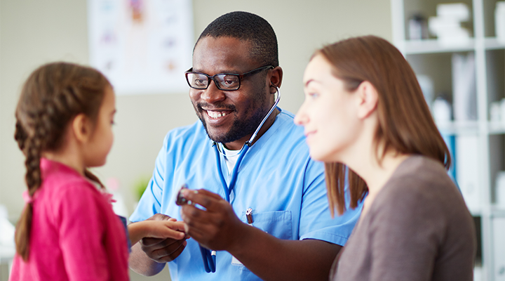 Doctor with stethoscope examining child with mother in foreground