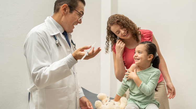 mother and doctor talking and smiling to little girl building confidence before being injected or vaccinated. Pediatrician holding a syringe about to put an injection to a child or kid mother and doctor talking and smiling to little girl building confidence before being injected or vaccinated. Pediatrician holding a syringe about to put an injection to a child or kid