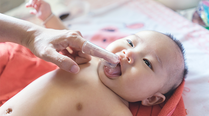 smiling infant with baby finger toothbrush
