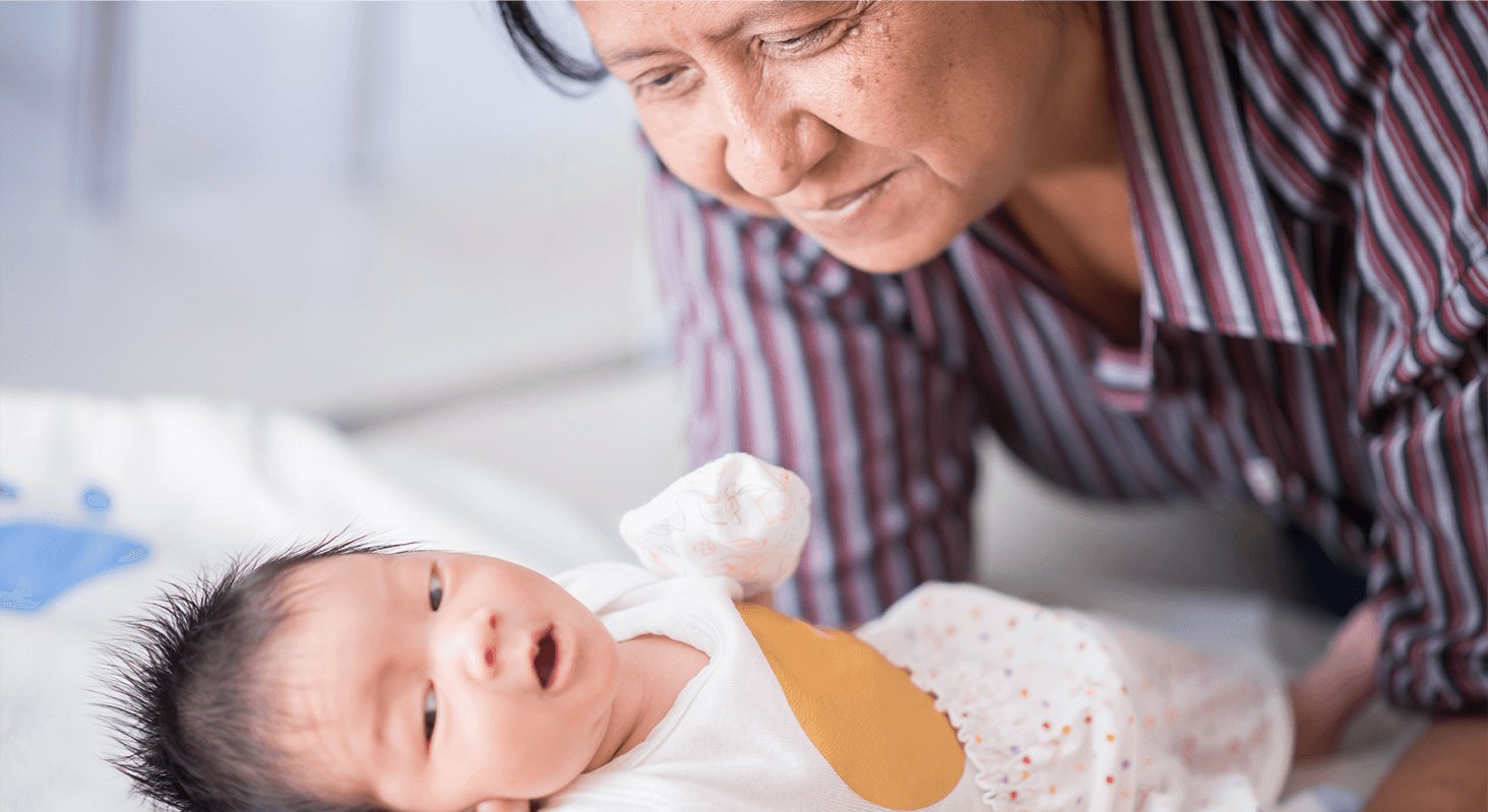 older caregiver smiling at baby laying on bed