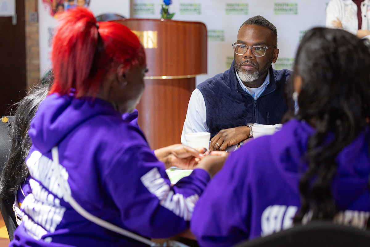 Mayor Brandon Johnson sitting with young women at a small table discussion.